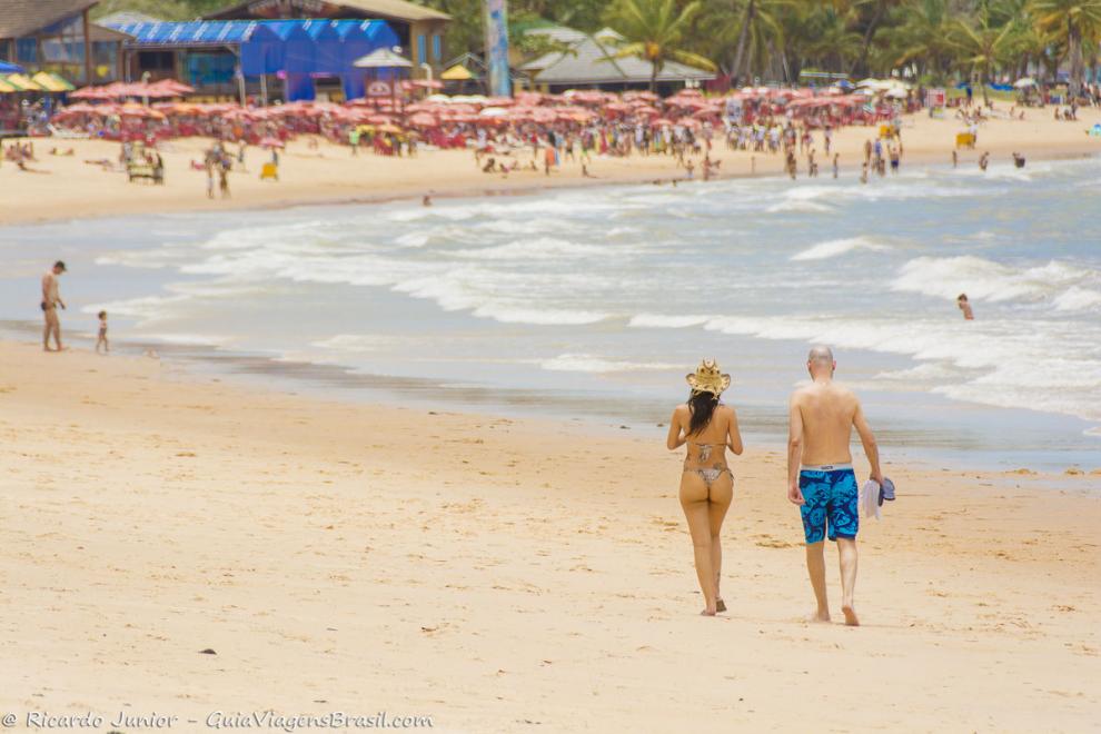 Imagem de um casal andando na beira do mar da Praia de Itacimirim.